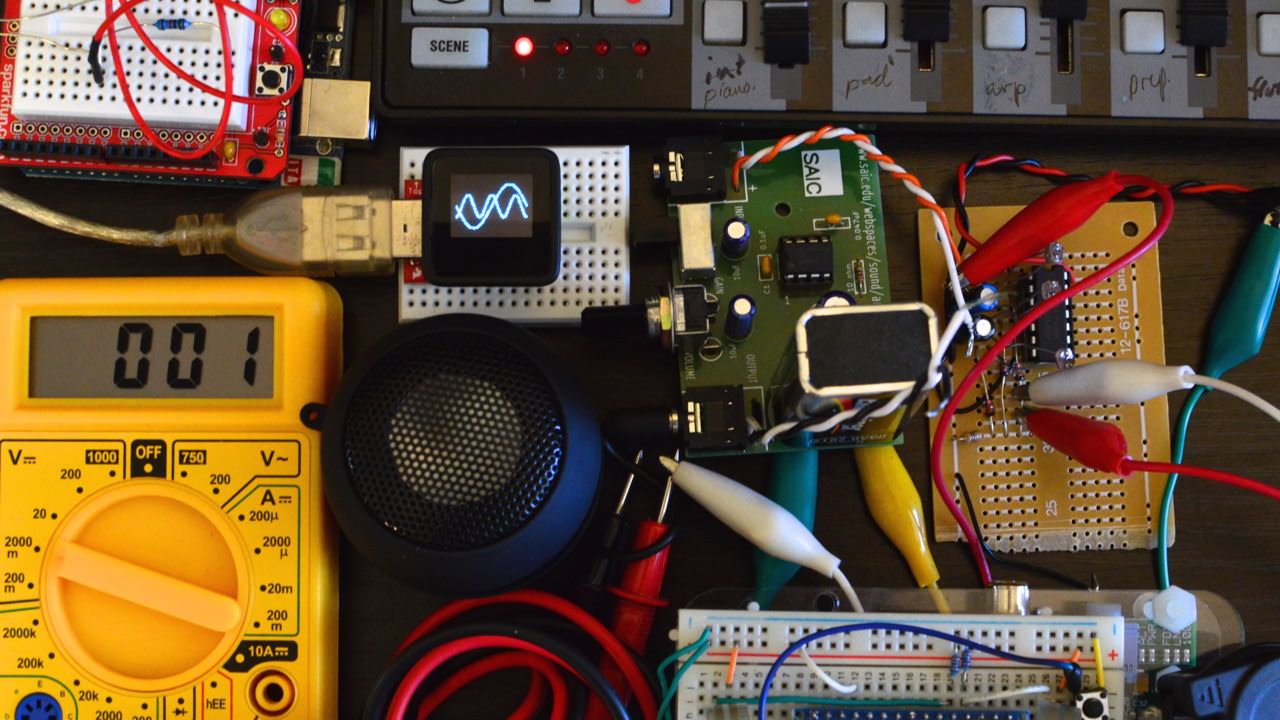Synths, circuits and parts on a desk.