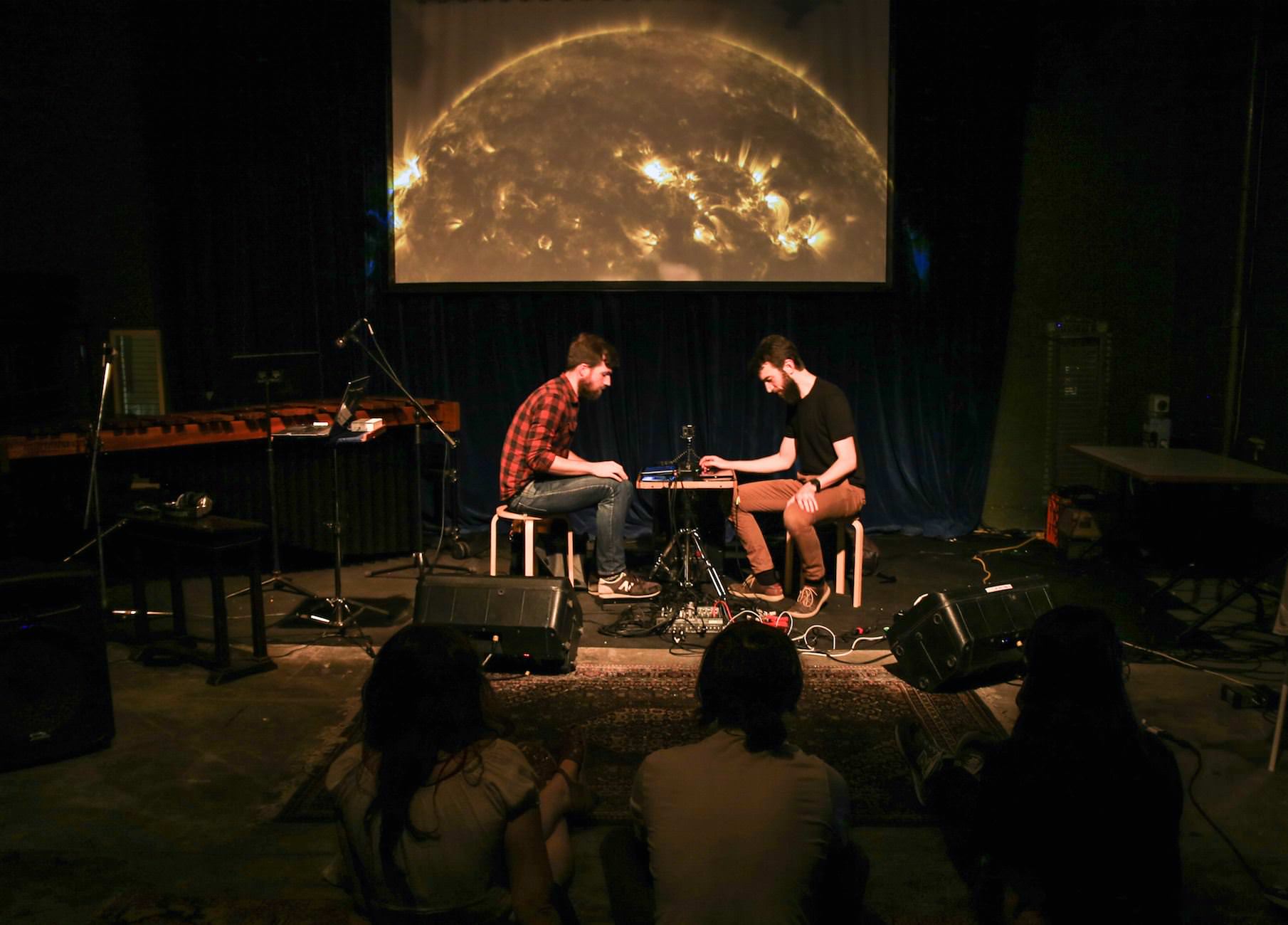 Alec and Charles performing on stage with astronomical images behind them.